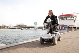 Dieses Foto zeigt eine Person im Rollstuhl am Hafen von Kappeln. Im Hintergrund sind die Schiffe der Schleischifffahrten zu sehen.